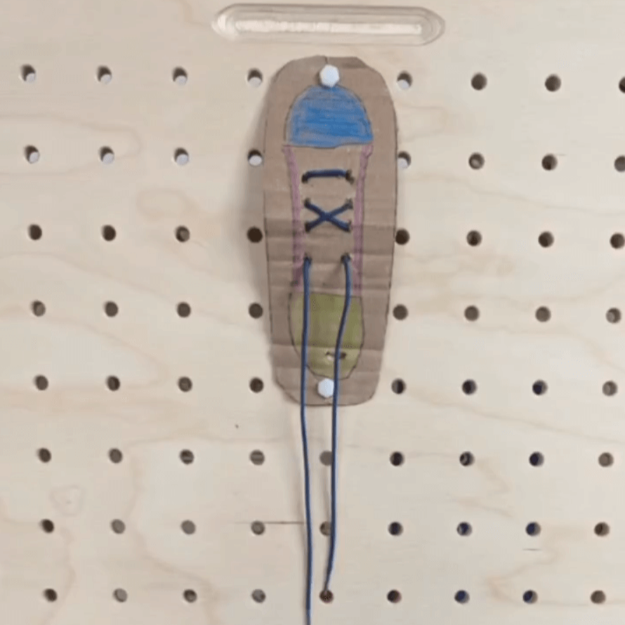 Befestige einen gebastelten Schuh mit Schuhbändern an der Lochplatte. VIel Spaß beim Schuhebinden lernen